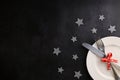 White plate with cutlery tied with red festive ribbon, grey glitter stars round the plate. Place for text