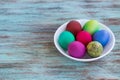 White plate of Easter versicolored eggs on wooden background