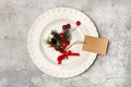 A white plate with fir branch, hollies and a cardboard label on a cement background