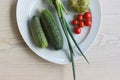 White Plate with fresh vegetables on wooden table. Two cucumbers, red cherry tomatoes, green cracked tomato with vertical splits, Royalty Free Stock Photo