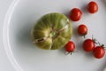 White Plate with fresh vegetables on wooden table. Two cucumbers, red cherry tomatoes, green cracked tomato with vertical splits, Royalty Free Stock Photo