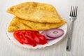Plate with fried cheburek, sweet pepper and red onion, fork on wooden table