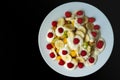 White plate with fruits, banana, raspberry, kiwi, apple and yogurt on a black background Royalty Free Stock Photo