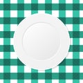 White plate on a green checkered tablecloth. Empty dish on a kitchen table cloth.