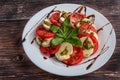 White plate of healthy classic delicious caprese salad with tomatoes and mozzarella cheese with basil leaves and strips of soy