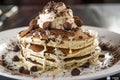 A white plate holds a tower of pancakes smothered in whipped cream and scattered with chocolate chips, creating a mouth