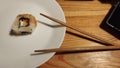 a white plate with a Japanese rice roll with fish, wooden Japanese chopsticks, and a small black bowl with soy sauce on the side Royalty Free Stock Photo