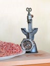 White plate with mince and vintage manual meat grinder turned upside down on a wooden cutting board on a beige background, front v Royalty Free Stock Photo