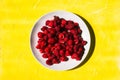 White plate with raspberries on a yellow background with texture. Fresh red berry with vitamins Royalty Free Stock Photo