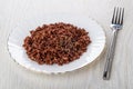 White plate with red boiled rice, fork on wooden table