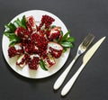 On white plate a ripe broken pomegranate fruit, fork and knife on a black background.