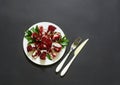 On white plate a ripe broken pomegranate fruit, fork and knife isolated on a black background.