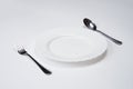 A white plate with silver fork and spoon isolated on white background with copy space. Dinner place setting. Table Setting. Royalty Free Stock Photo