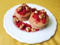 A white plate with stacks of pancakes with red currant and walnuts