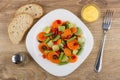 White plate with vegetable mix, bowl with sauce, bread, pepper