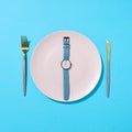 White plate with whatch shows six o`clock served knife and fork on a blue background and shadows. Time to eat and diet Royalty Free Stock Photo