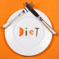 White plate with word diet made of pieces of vegetables on orange tablecloth background. Fork and knife lying on it.