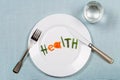 White plate with word health made of colorful pieces of vegetables and glass of pure on blue teblecloth background.