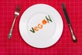 White plate with word vegan made of pieces of vegetables on red