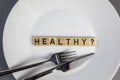 White plate with the words Healthy and a question mark top view with fork and knife, medical health and food concept