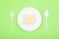 White plate with yellow gift box, spoon, fork on green background. Festive, birthday, Gift pastel minimal background