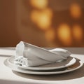 White plates stacked neatly, topped with a folded white cloth napkin on a table. Warm Royalty Free Stock Photo