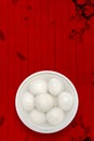 A white porcelain bowl of rice balls is placed on a traditional auspicious cloud, plum, and wooden board texture background.