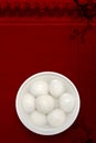 A white porcelain bowl of rice balls is placed on a traditional auspicious cloud, plum, and wooden board texture background.