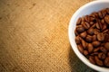 White cup of coffee beans on burlap background with space for text Royalty Free Stock Photo