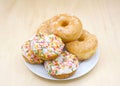 porcelain plate with glazed and frosted cake donuts with sprinkles on a light wood table Royalty Free Stock Photo