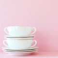Stack of white tea cups and saucers creating a minimalist aesthetic on pink background Royalty Free Stock Photo