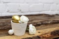 White pot with decorative bunny, roses and Easter golden eggs on brown wooden table and white bricked background. Easter rabbit, Royalty Free Stock Photo
