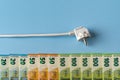 White power plug above row of euro money banknotes against blue background. Concept of rising energy bills and electricity price Royalty Free Stock Photo