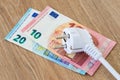 White power plug over euro banknotes on a brown wooden surface. Expensive energy and cost of electricity concepts