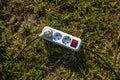 White power strip with red switch and black cable on green grass under sunlight Royalty Free Stock Photo