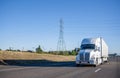 White powerful long haul big rig semi truck with dry van semi trailer moving on the straight wide highway road with hillside Royalty Free Stock Photo