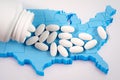 White prescription pills spilling from medicine bottle over map of America