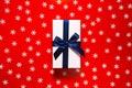 White present box with dark blue ribbon and bow on red background with decorative snowflakes. Christmas gift concept. Festive and Royalty Free Stock Photo