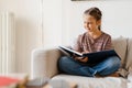 White preteen girl smiling and reading book while sitting on couch Royalty Free Stock Photo