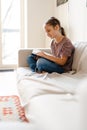 White preteen girl smiling and reading book while sitting on couch Royalty Free Stock Photo