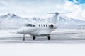 White private jet taxiing on airport taxiway in winter on the background of high picturesque snow capped mountains