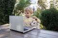 White puppy and toddler boy stands in front of open laptop in garden