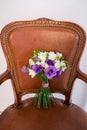 White and purple bridal bouquet on a brown chair.