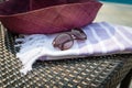 A white and purple Turkish towel, sunglasses and straw hat on rattan lounger with a blue swimming pool as background. Royalty Free Stock Photo