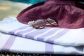 A white and purple Turkish towel, sunglasses and straw hat on rattan lounger with a blue swimming pool as background. Royalty Free Stock Photo