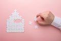 White puzzle. House shape puzzle. The concept of rent, mortgage. Hand holding piece of white puzzle. Pink background Royalty Free Stock Photo