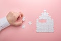 White puzzle. House shape puzzle. The concept of rent, mortgage. Hand holding piece of white puzzle. Pink background Royalty Free Stock Photo