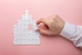 White puzzle. House shape puzzle. The concept of rent, mortgage. Hand holding piece of white puzzle. Pink background Royalty Free Stock Photo