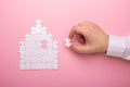 White puzzle. House shape puzzle. The concept of rent, mortgage. Hand holding piece of white puzzle. Pink background Royalty Free Stock Photo