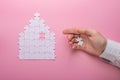 White puzzle. House shape puzzle. The concept of rent, mortgage. Hand holding piece of white puzzle. Pink background Royalty Free Stock Photo